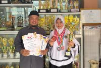 AZ Syahra Nastiti Ramadhani didampingi Kepsek Muhlisari S.Pd menunjukkan piagam dan piala prestasi setelah meraih juara 2 Mapel Matematika se-Madura dalam Lomba Matematika GCO 2026, membuktikan kerja keras dan dedikasinya dalam mengembangkan potensi akademik.