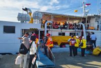 Petugas pelabuhan membantu penumpang menaiki kapal, memastikan perjalanan mudik gratis berjalan lancar dan aman.