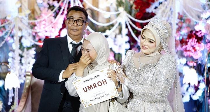 Ket Foto: Penerima hadiah paket umrah menangis haru saat nomor undiannya dibacakan langsung oleh H. Bambang Budianto. Momen penuh haru tersebut diapit kedua mempelai, H. Bambang Budianto dan Hj. Dian Mariana, dalam resepsi pernikahan di Banyuwangi.